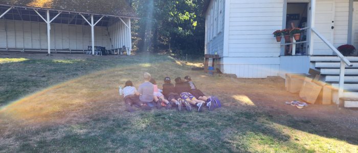 Learners reading on the grass out front of the schoolhouse